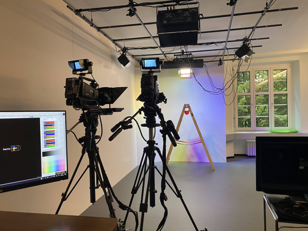 TV-Studio, zwei Kameras, farbig beleuchteter Hintergrund