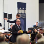 Beni Thurnheer spricht mit dem Publikum, im Hintergrund ist das Orchester und der Dirigent zu sehen.