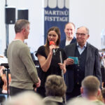Alex Frei, Zofia Neugebauer, Beni Thurnheer stehen vor dem Orchester. Zofia Neugebauer spricht in ein Mikrofon Bild: Benno Hunziker