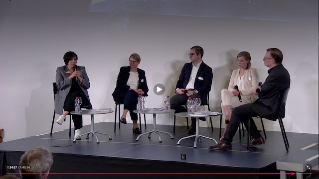 Diskussion auf dem Podium. 5 Teilnehmende sitzen nebeneinander und sprechen in ein Mikrofon.